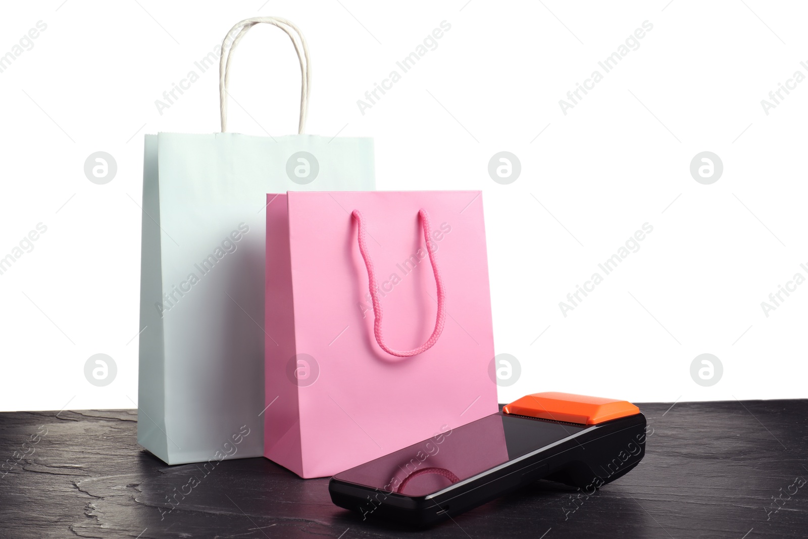 Photo of Payment terminal and shopping bags on black table against white background