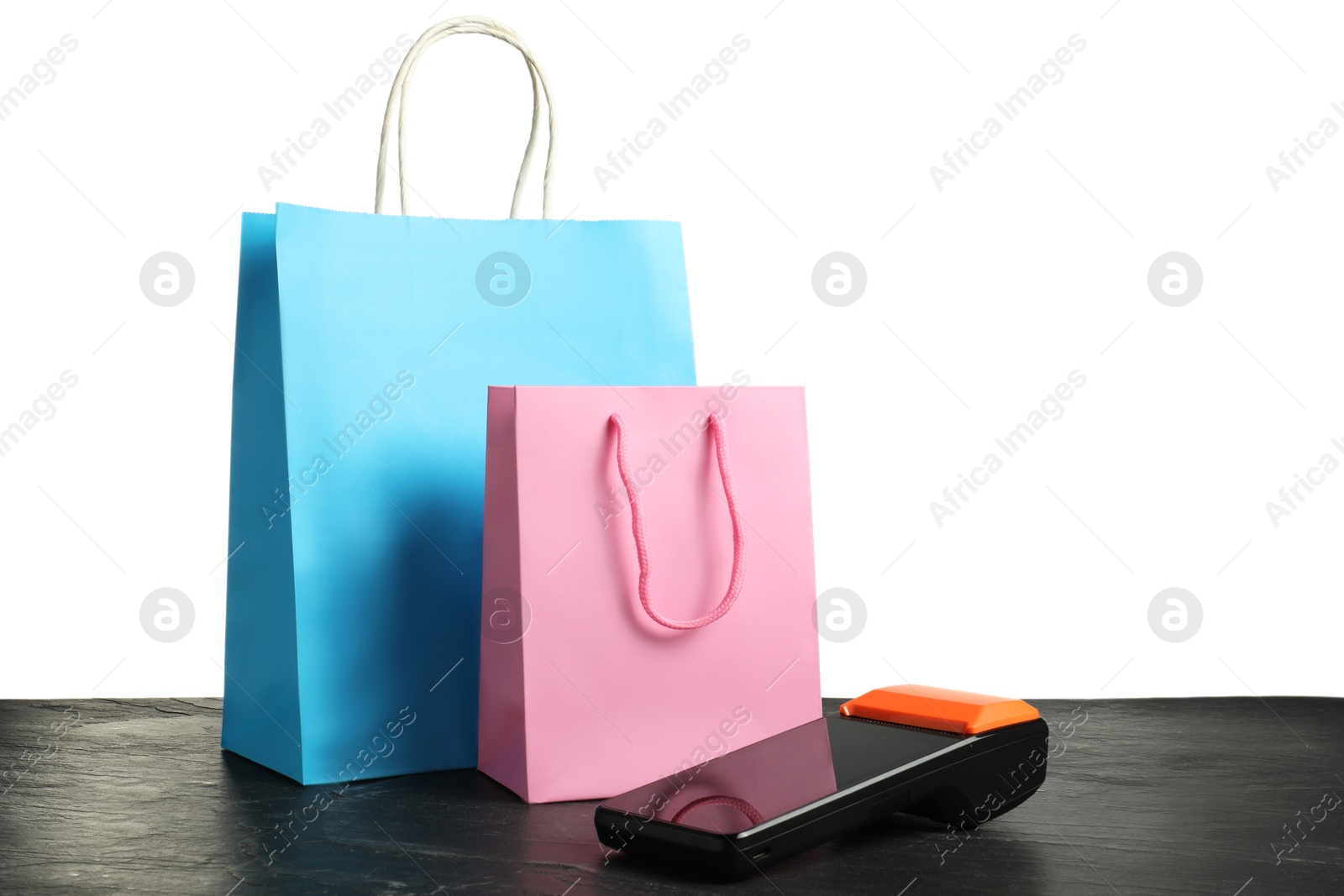 Photo of Payment terminal and shopping bags on black table against white background