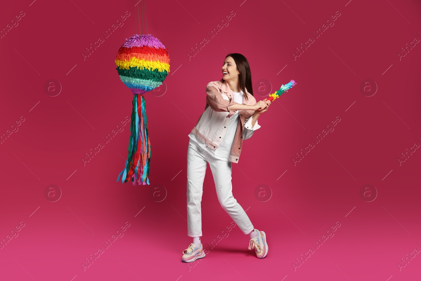 Photo of Happy woman breaking colorful pinata with stick on pink background