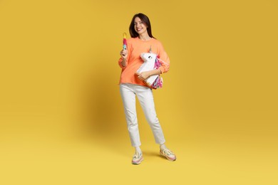 Happy woman with unicorn shaped pinata and stick on yellow background