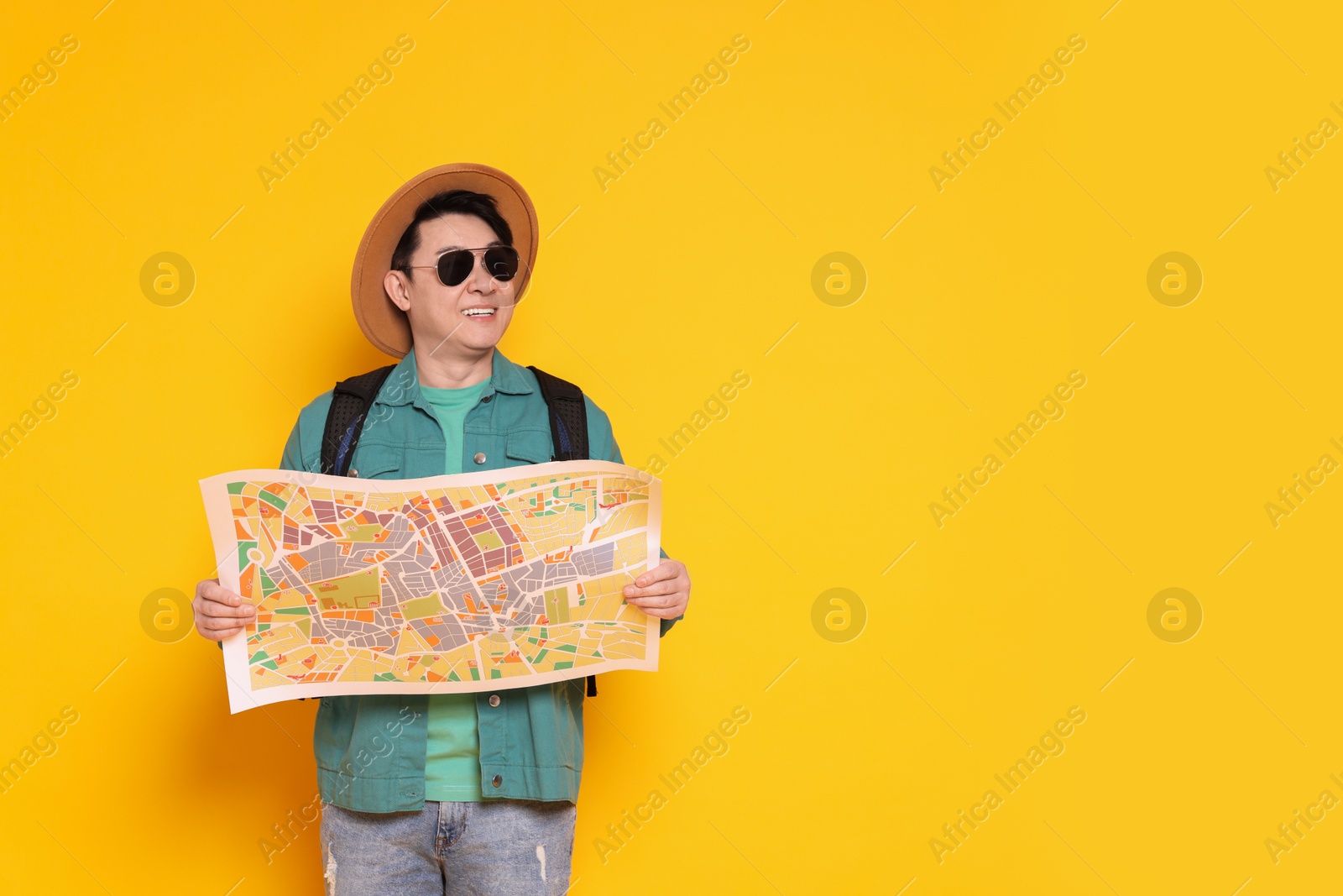 Photo of Traveller with map and backpack on yellow background. Space for text