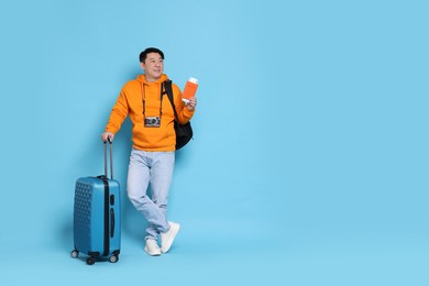 Photo of Happy traveller with passport, suitcase and camera on light blue background. Space for text