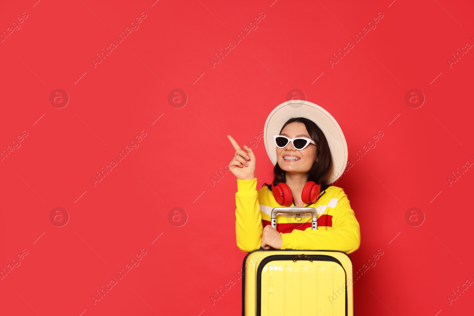 Photo of Happy traveller with suitcase pointing at something on red background. Space for text