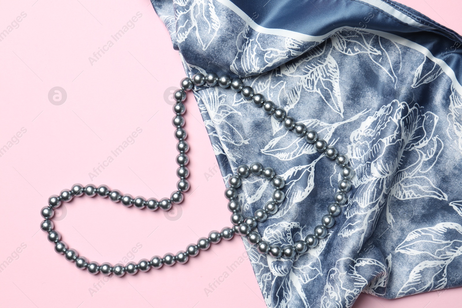 Photo of Beautiful scarf and pearl necklace on light pink background, top view. Stylish accessories