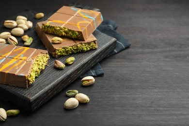 Photo of Pieces of Dubai chocolate bars with pistachios and knafeh on black wooden table, closeup. Space for text