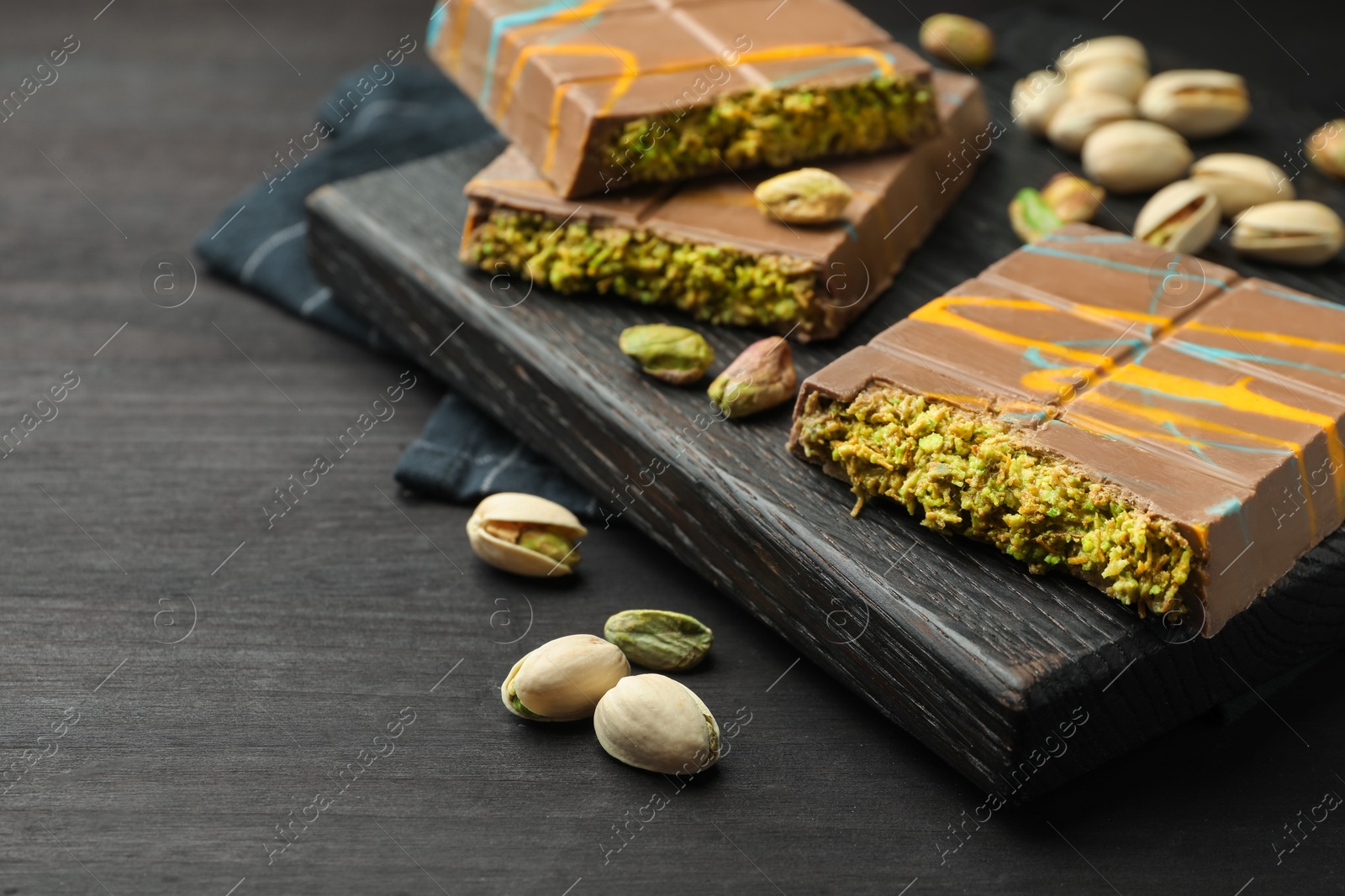 Photo of Pieces of Dubai chocolate bars with pistachios and knafeh on black wooden table, closeup