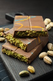 Photo of Pieces of Dubai chocolate bars with pistachios and knafeh on black table, closeup