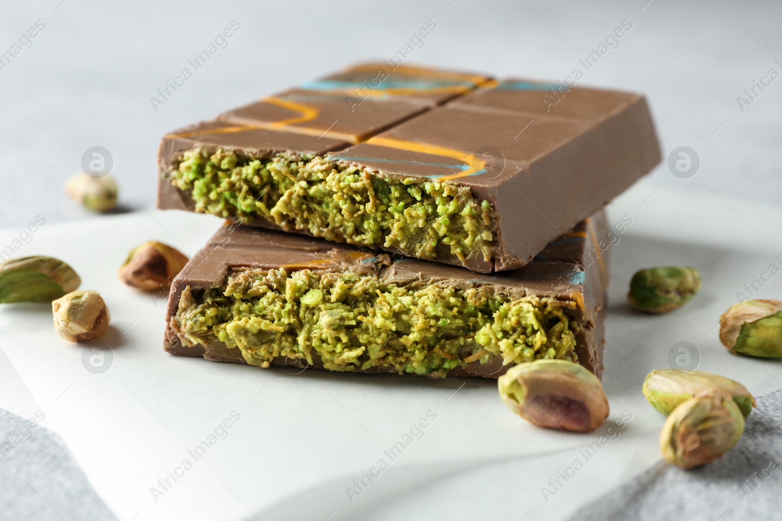 Photo of Pieces of Dubai chocolate bar with pistachios and knafeh on light grey table, closeup