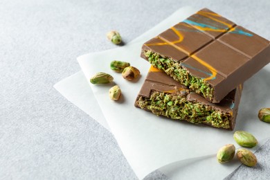 Photo of Pieces of Dubai chocolate bar with pistachios and knafeh on light grey table, closeup. Space for text