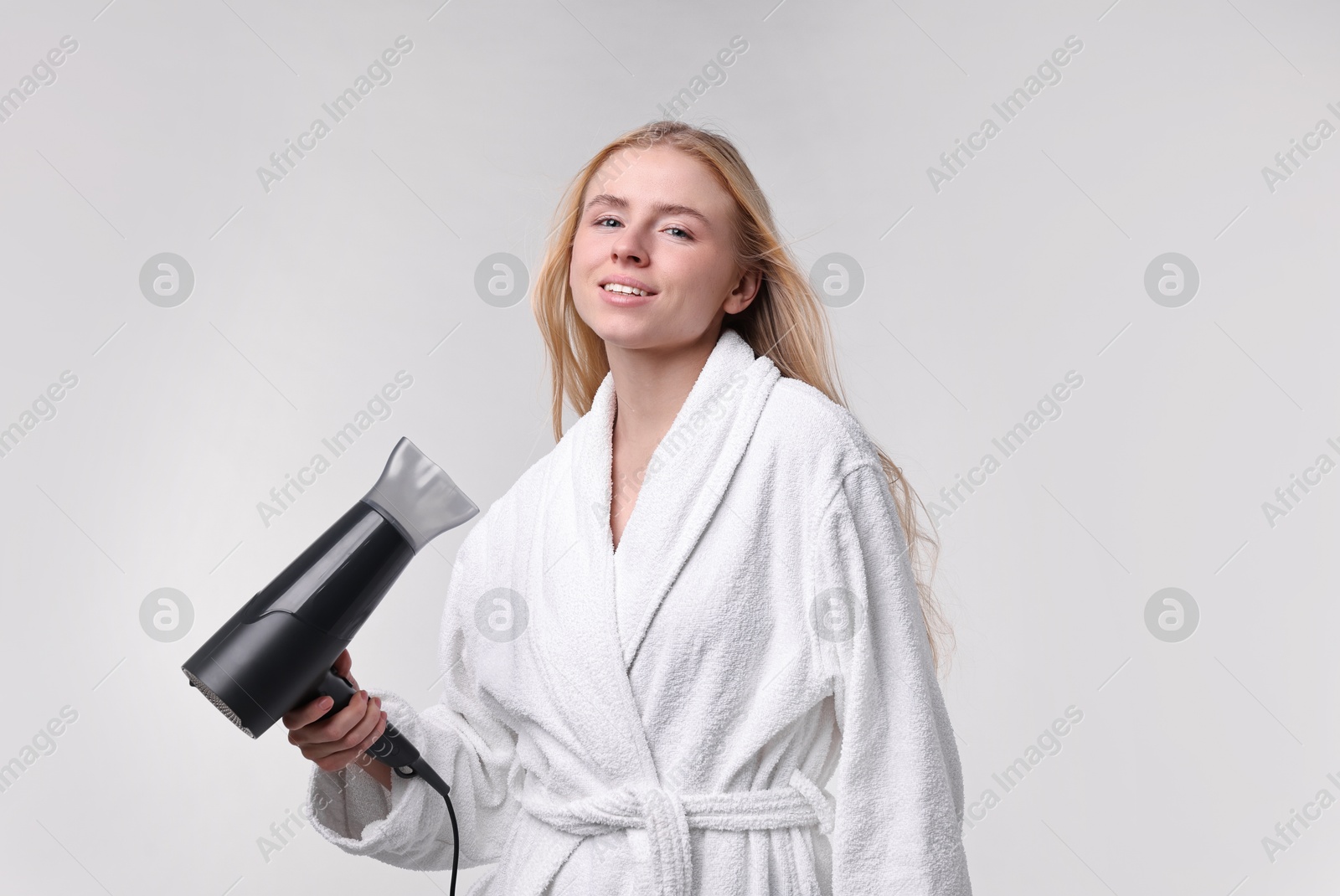 Photo of Beautiful young woman drying her hair with hairdryer on light grey background