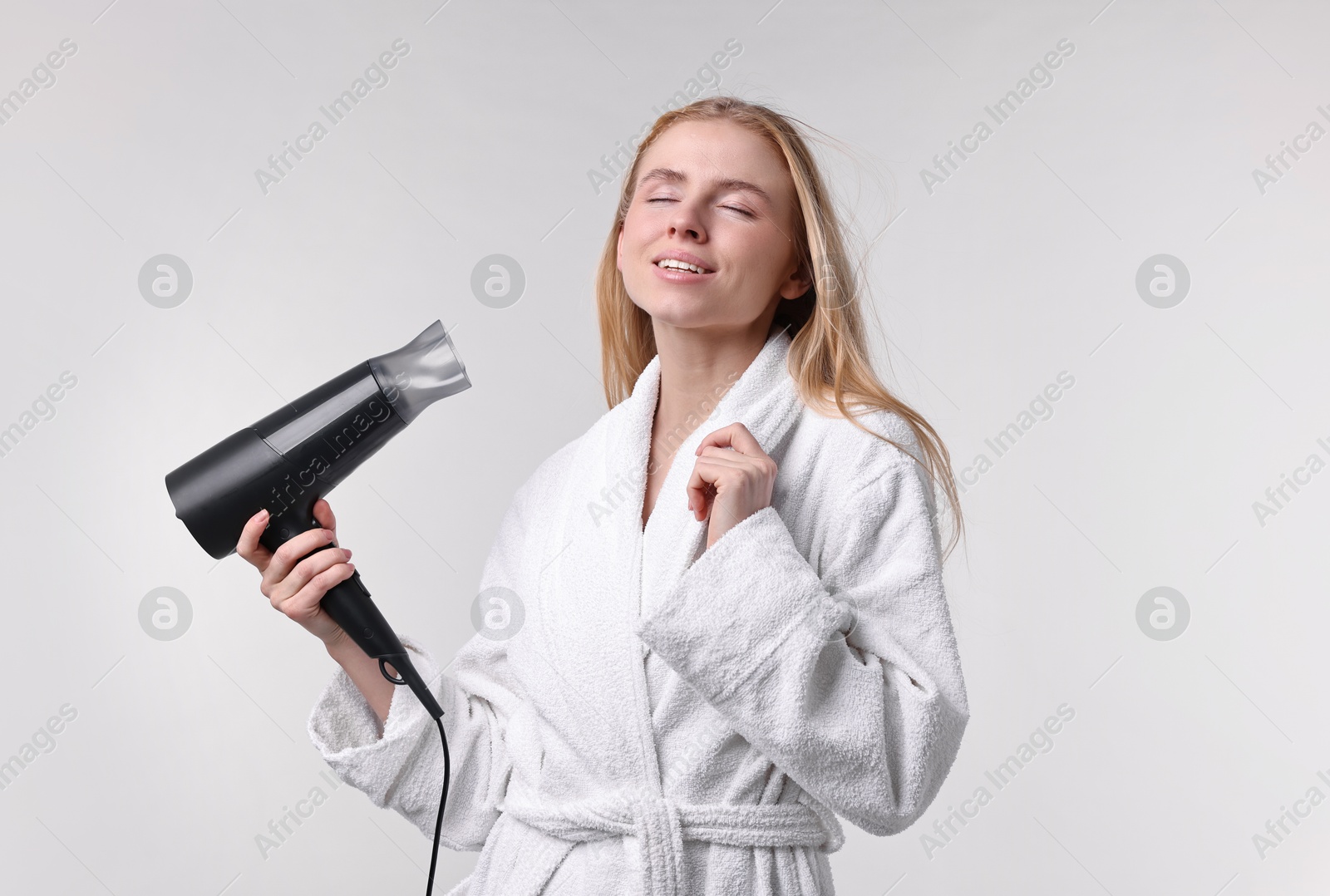 Photo of Beautiful young woman drying her hair with hairdryer on light grey background