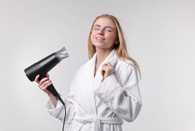 Photo of Beautiful young woman drying her hair with hairdryer on light grey background