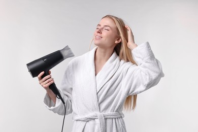 Photo of Beautiful young woman drying her hair with hairdryer on light grey background