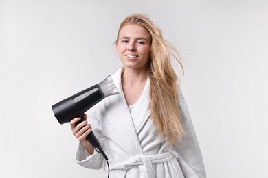 Photo of Beautiful young woman drying her hair with hairdryer on light grey background