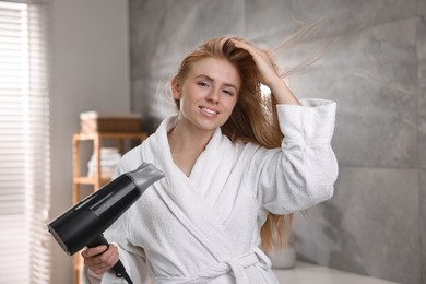 Photo of Beautiful young woman drying her hair in bathroom