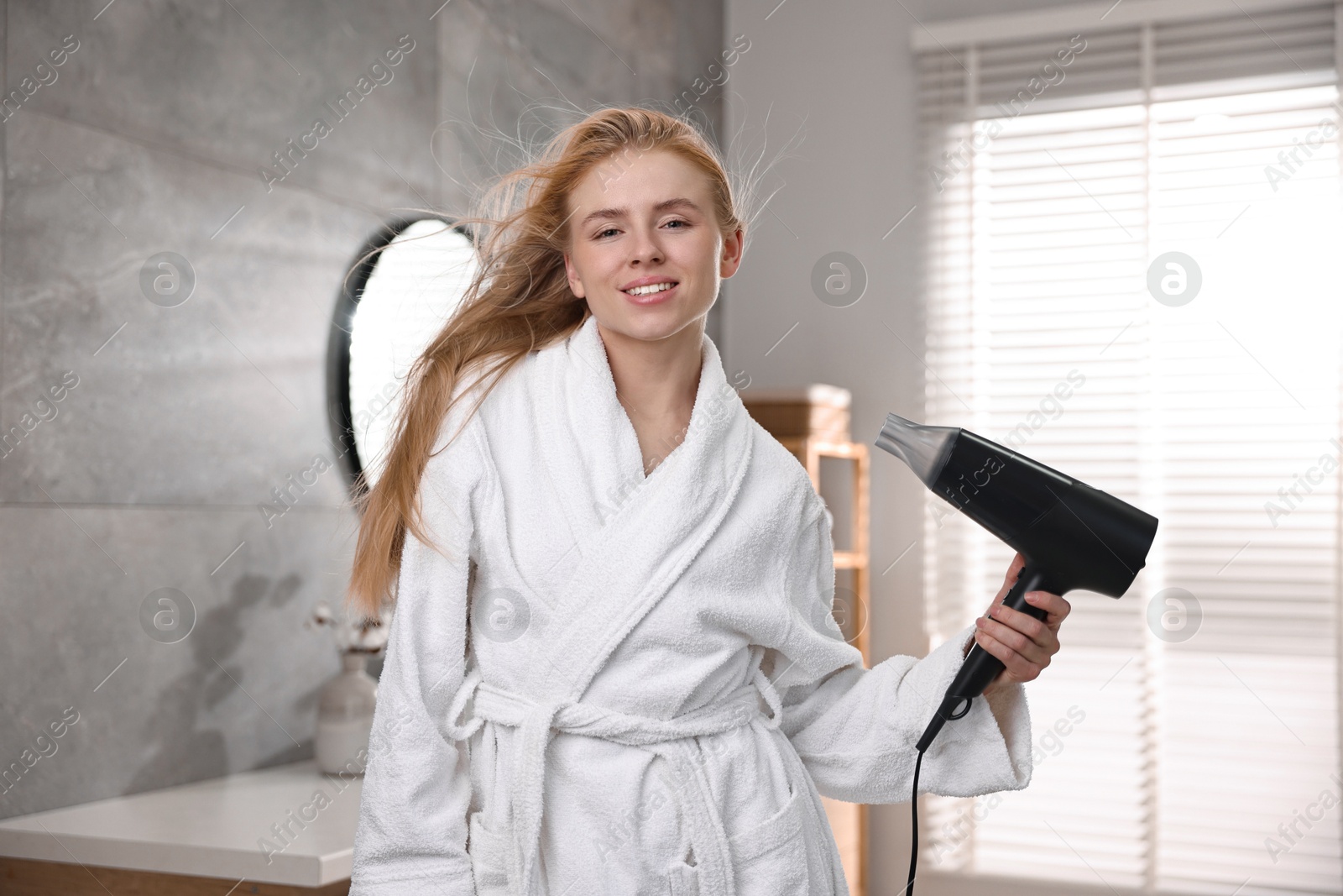 Photo of Beautiful young woman drying her hair in bathroom