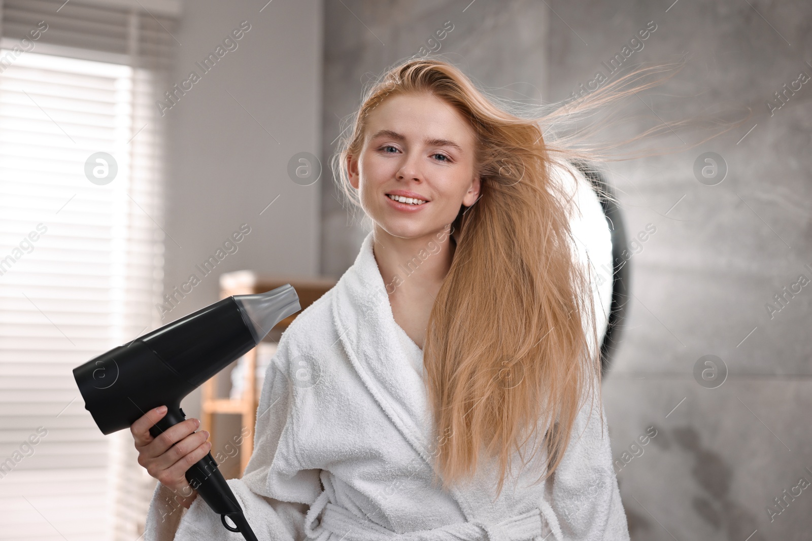 Photo of Beautiful young woman drying her hair in bathroom