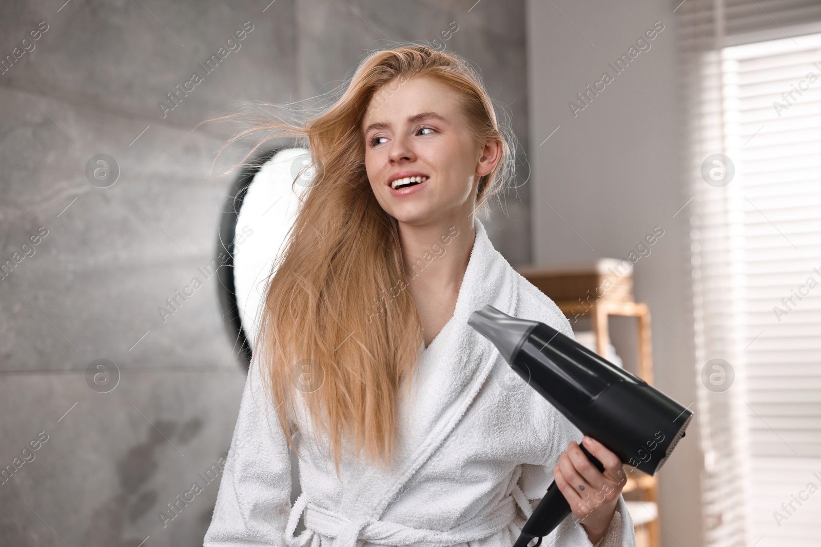 Photo of Beautiful young woman drying her hair in bathroom