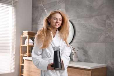 Beautiful young woman drying her hair in bathroom