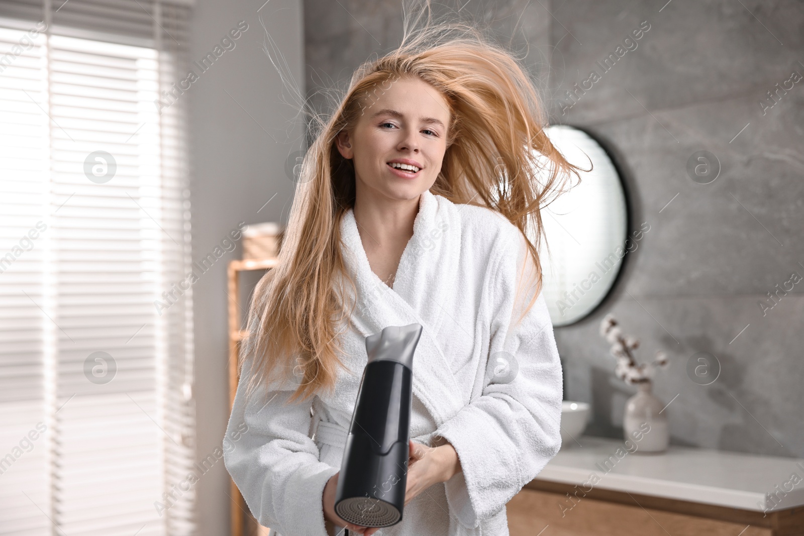 Photo of Beautiful young woman drying her hair in bathroom