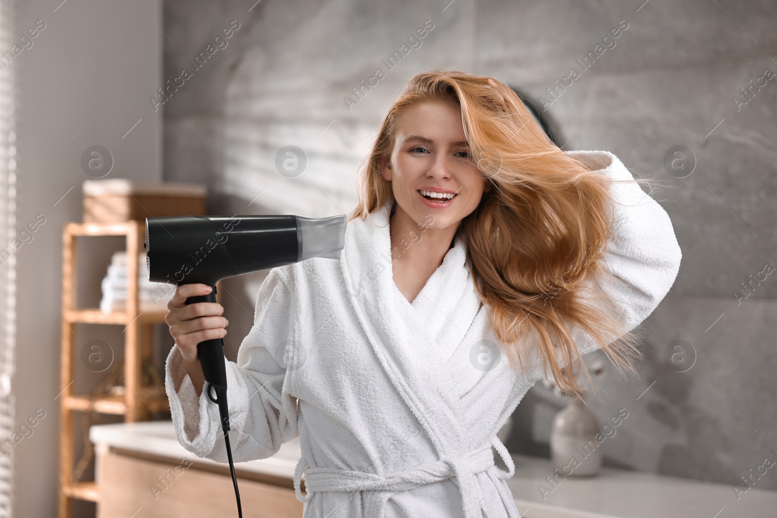 Photo of Beautiful young woman drying her hair in bathroom