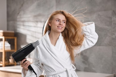 Photo of Beautiful young woman drying her hair in bathroom