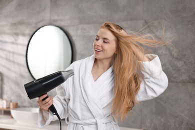 Photo of Beautiful young woman drying her hair in bathroom