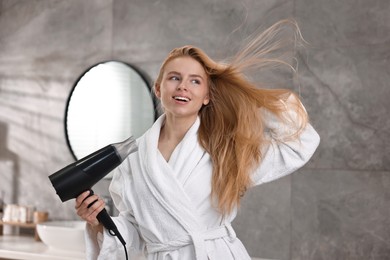 Photo of Beautiful young woman drying her hair in bathroom