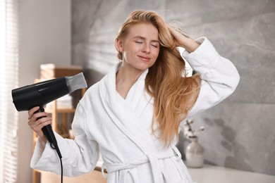 Photo of Beautiful young woman drying her hair in bathroom