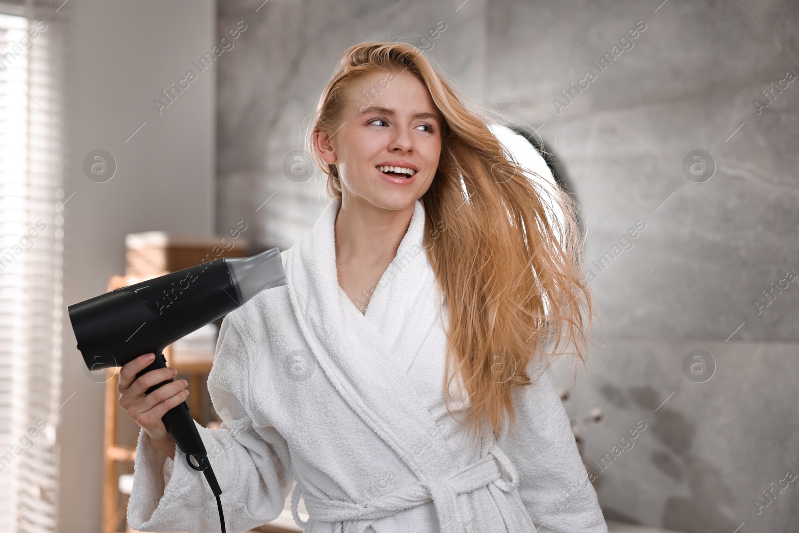 Photo of Beautiful young woman drying her hair in bathroom