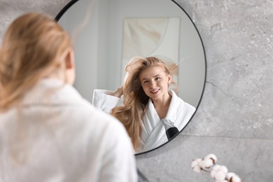 Photo of Beautiful young woman drying her hair near mirror in bathroom