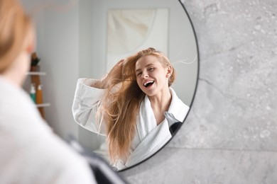 Photo of Beautiful young woman drying her hair and singing near mirror in bathroom