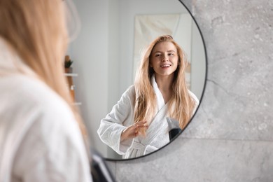 Photo of Beautiful young woman drying her hair near mirror in bathroom