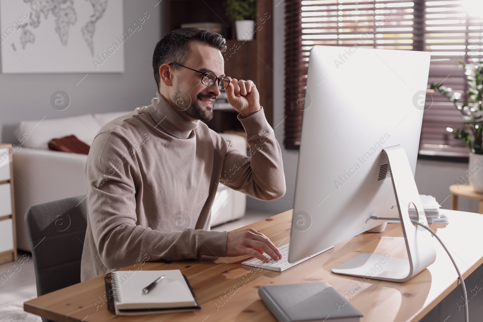 Photo of Happy man working with computer at desk indoors. Home office