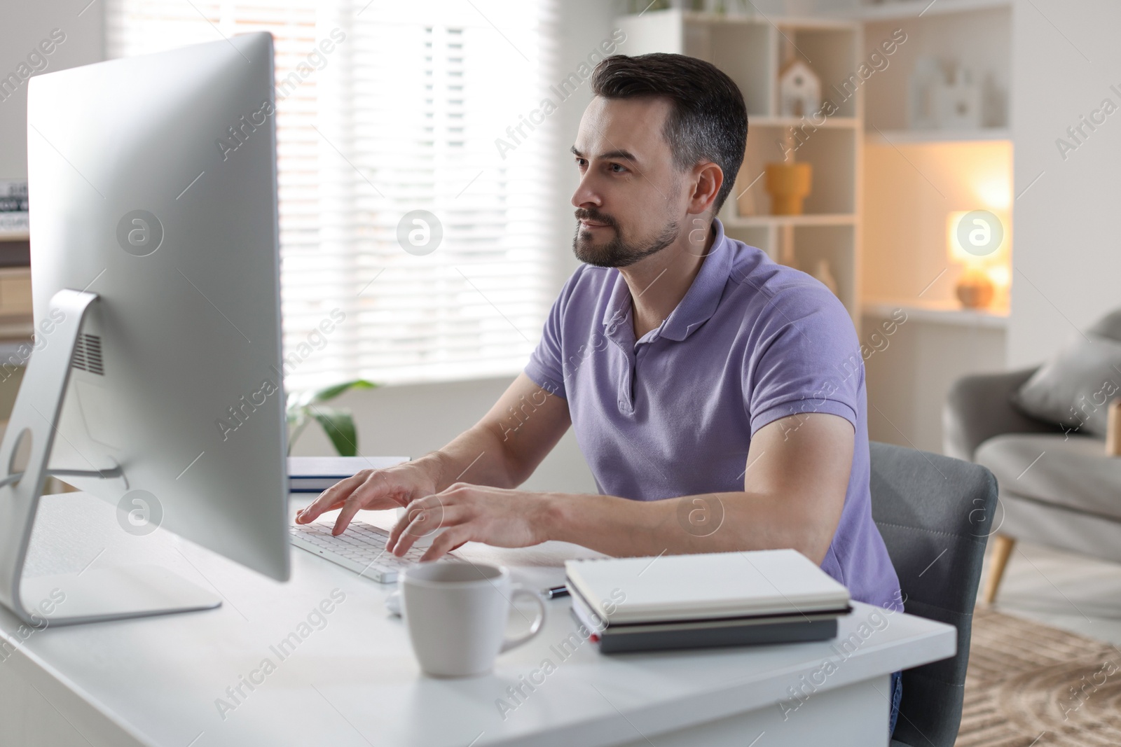 Photo of Handsome man working with computer at desk indoors. Home office