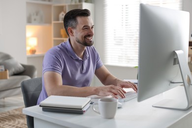 Photo of Happy man working with computer at desk indoors. Home office