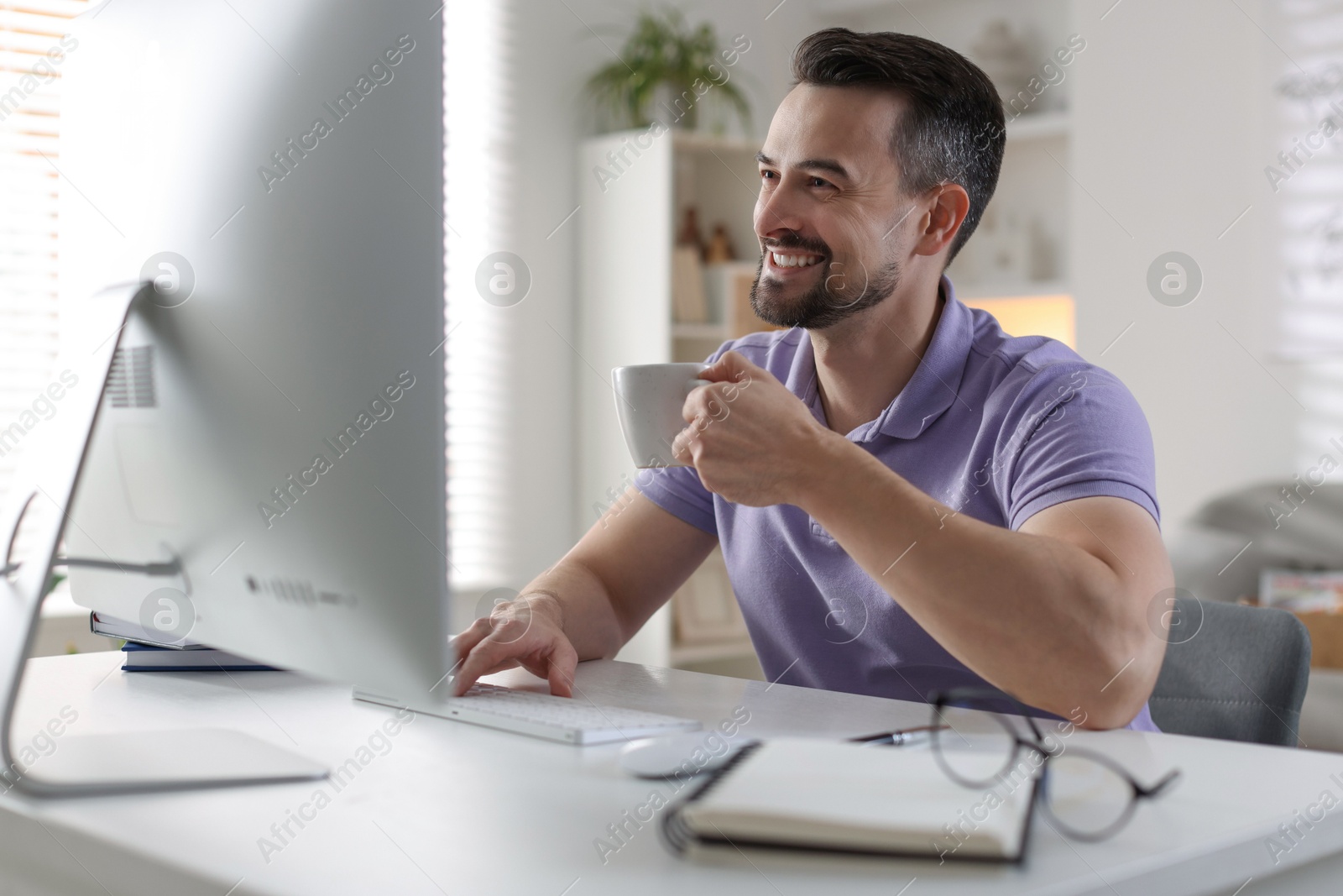 Photo of Happy man working with computer at desk indoors. Home office