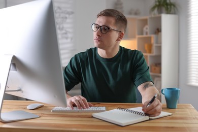 Photo of Handsome man working with computer at desk indoors. Home office