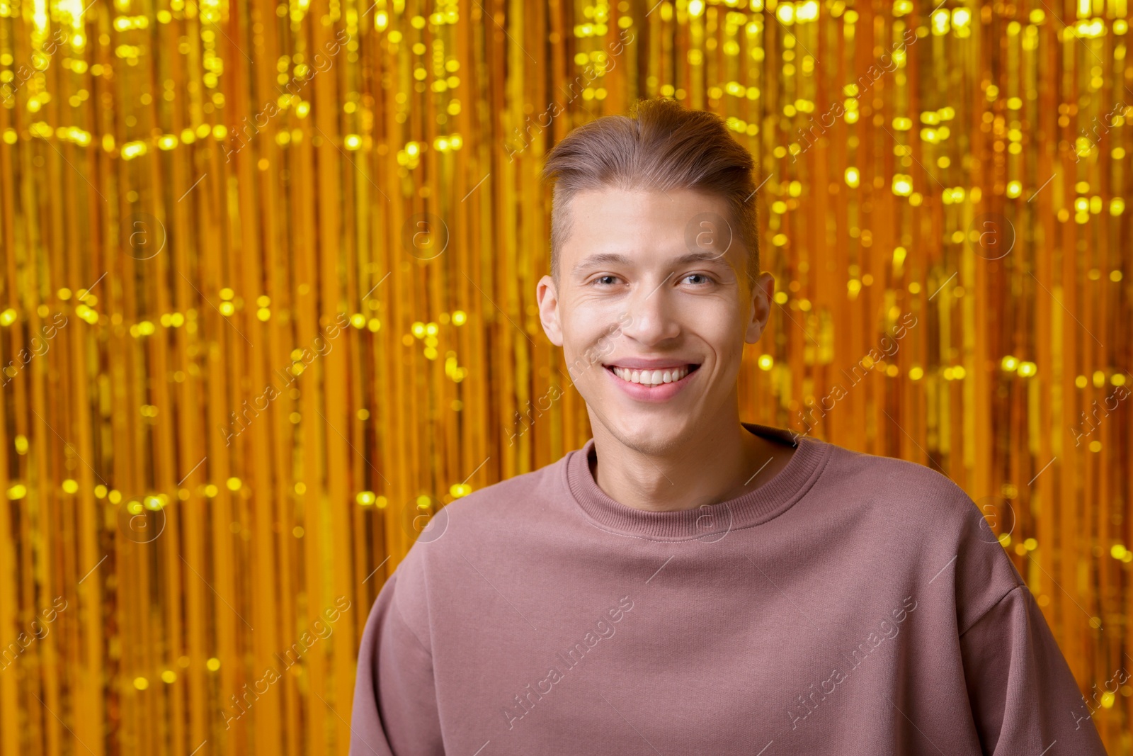 Photo of Happy young man against golden foil curtain. Space for text