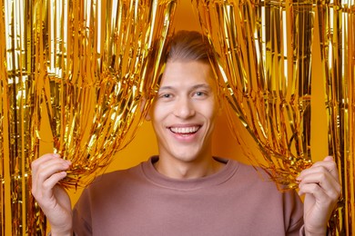 Photo of Happy young man looking out through golden foil curtain against orange background