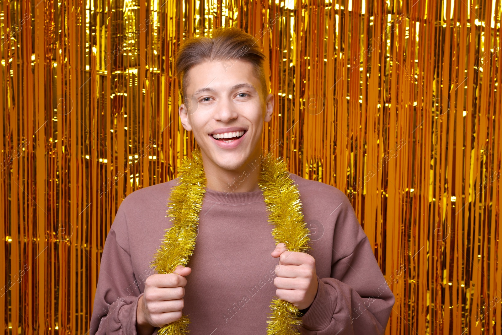 Photo of Happy young man with yellow tinsel against golden foil curtain