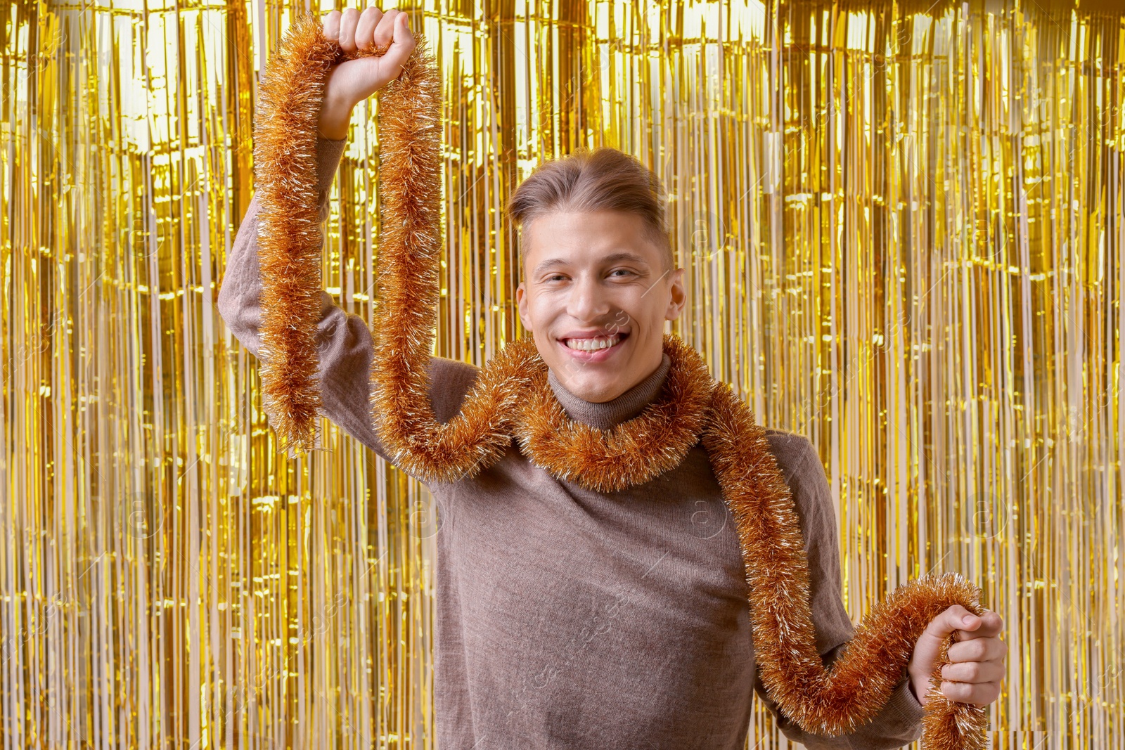 Photo of Happy young man with golden tinsel against foil curtain