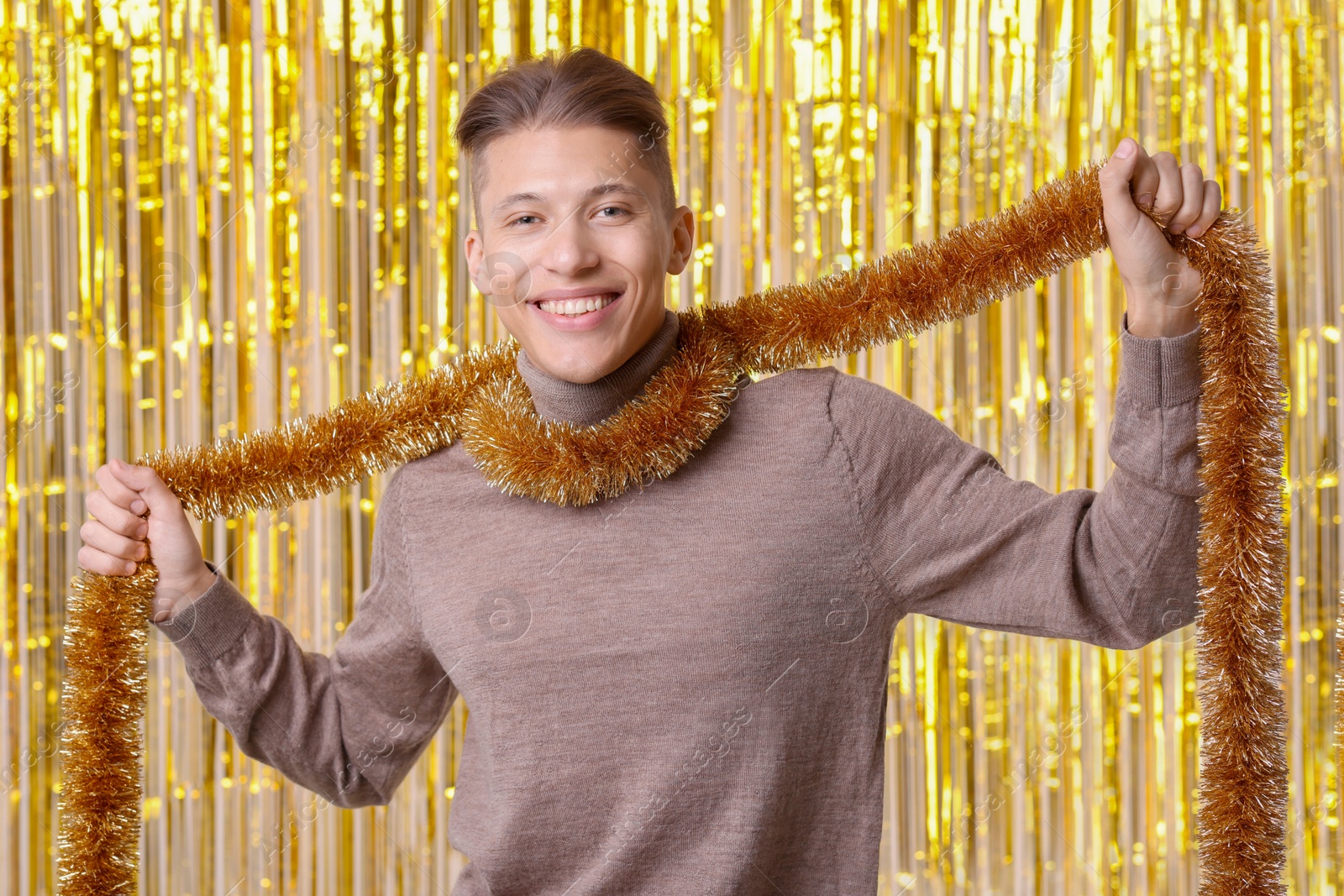 Photo of Happy young man with golden tinsel against foil curtain