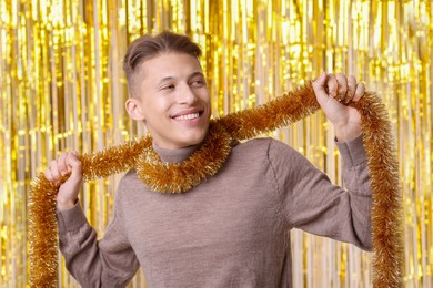 Photo of Happy young man with golden tinsel against foil curtain