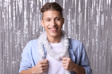 Photo of Happy young man with white tinsel against silver foil curtain