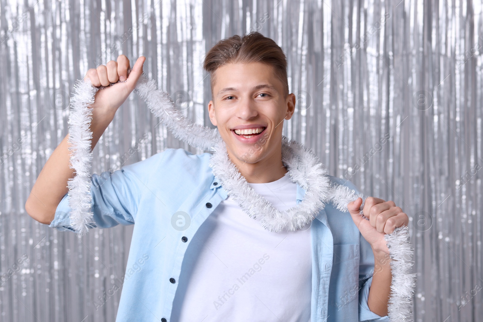 Photo of Happy young man with white tinsel against silver foil curtain