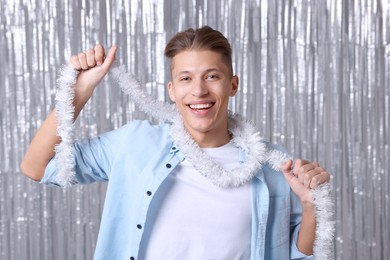 Happy young man with white tinsel against silver foil curtain