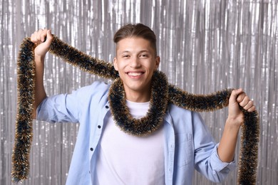 Photo of Happy young man with tinsel against silver foil curtain