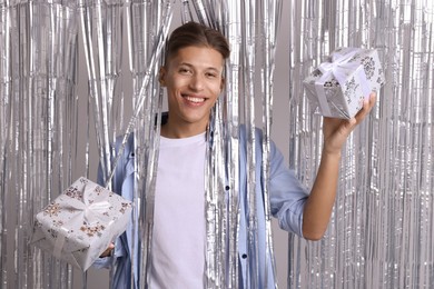 Photo of Happy young man with gift boxes near silver foil curtain against light background