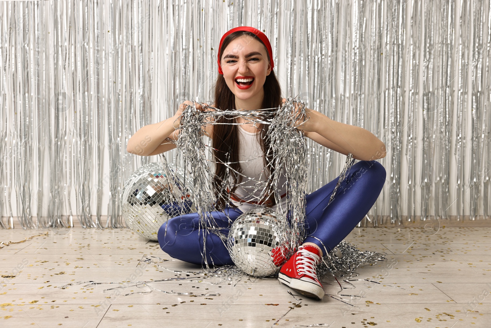 Photo of Emotional young woman in retro outfit with tinsel against silver foil curtain indoors